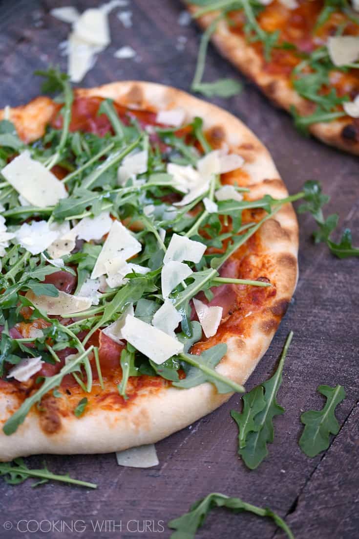 Pizza topped with prosciutto, arugula, shaved parmesan cheese, and tomato sauce.