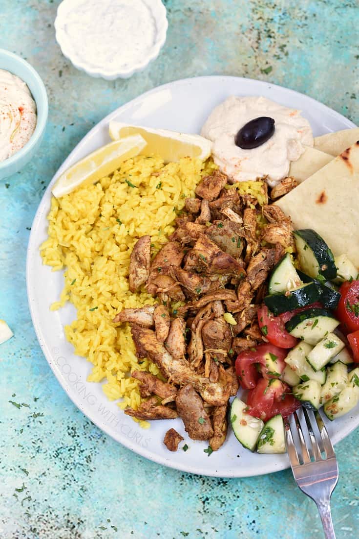 Instant Pot Chicken Shawarma on a white plate with Yellow Rice, Hummus, and Pita wedges, hummus, cucumber and tomato wedges.