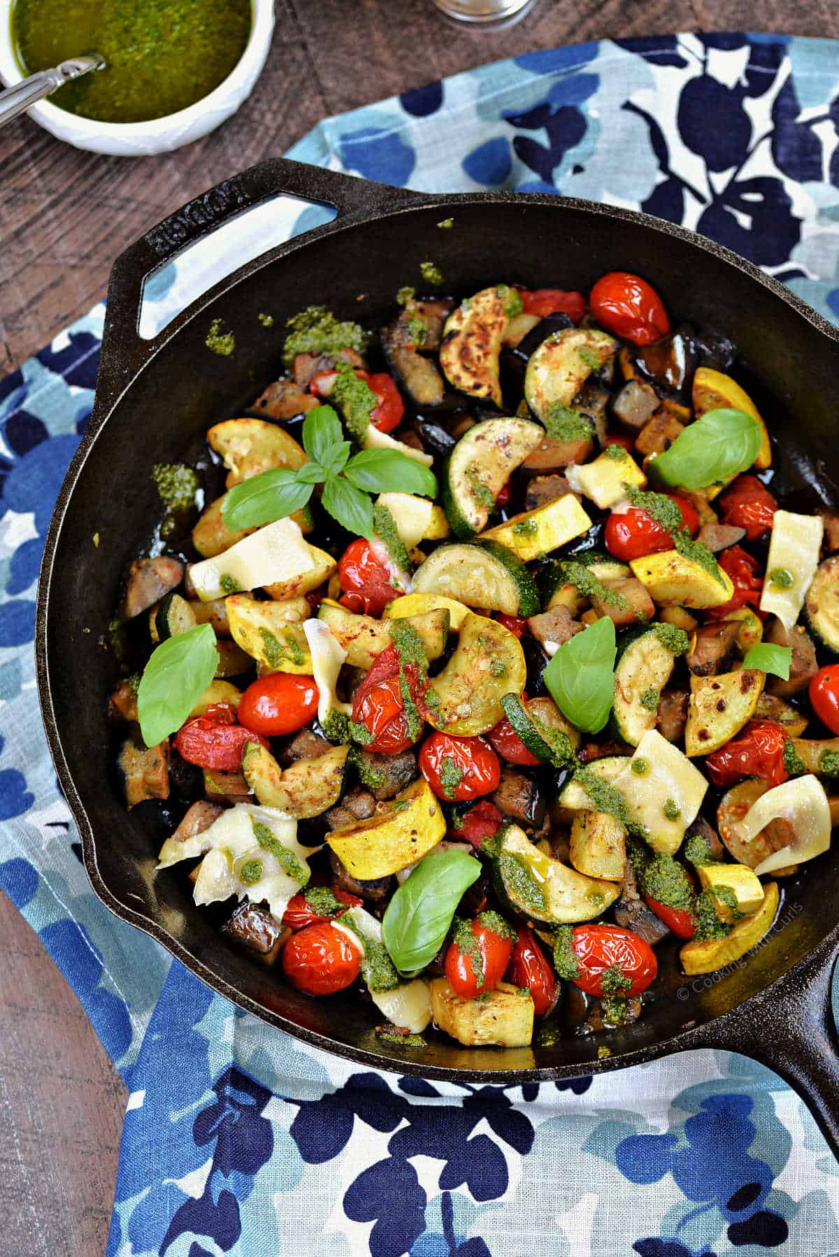 Charred summer vegetables with shaved cheese and fresh basil pistou in a cast iron skillet.