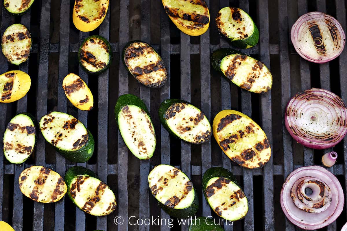 Charred slices of zucchini, summer squash and red onion on the grill. 