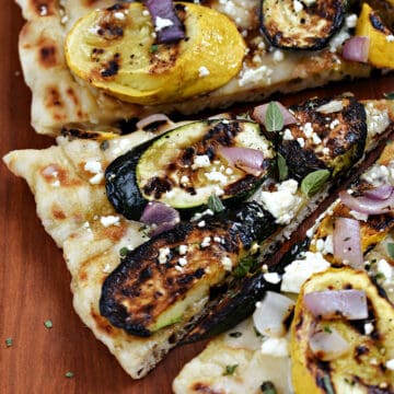 Five slices of grilled pizza topped with zucchini, summer squash, red onion and cheese.