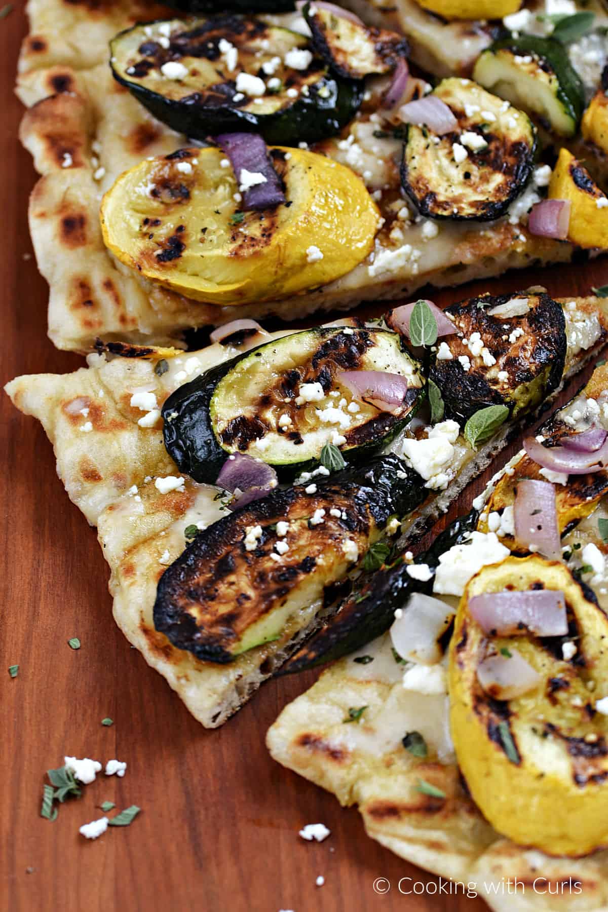 Five slices of grilled pizza topped with zucchini, summer squash, red onion and feta cheese. 