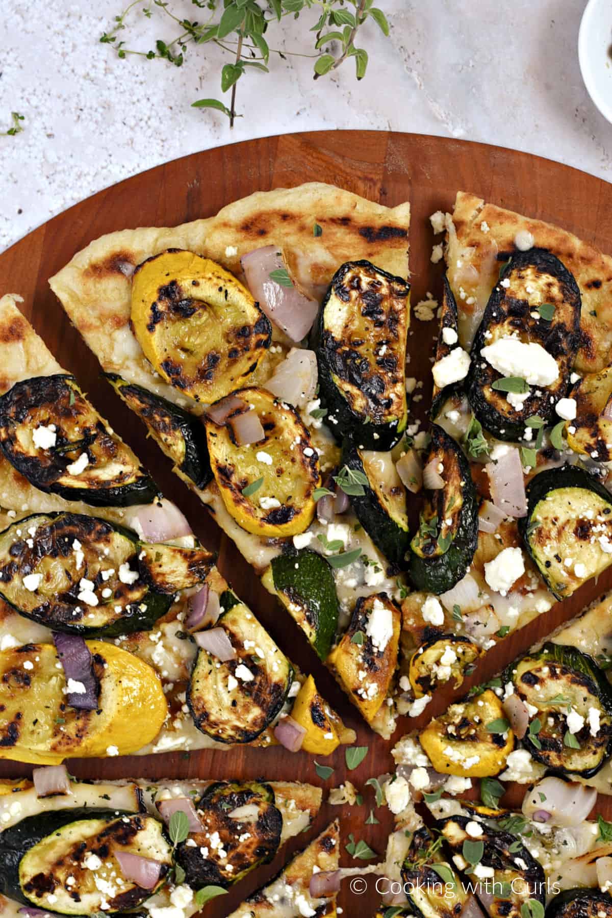 Looking down on grilled slices of summer squash, zucchini, and red onion on pizza topped with feta cheese. 