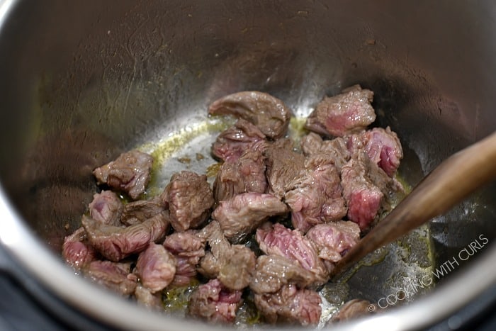 Brown the beef cubes in a hot pressure cooker.