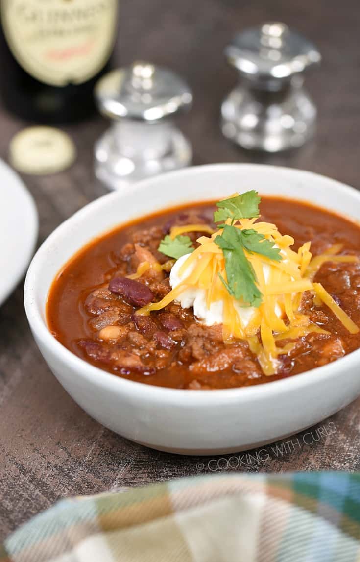 A bowl of chili topped with sour cream, shredded cheddar and cilantro leaves.