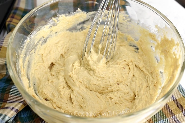 Donut batter mixed with a wire whisk in a large glass bowl.