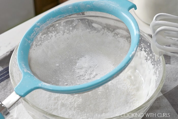 Powdered sugar being sifted into a large bowl cookingwithcurls.com