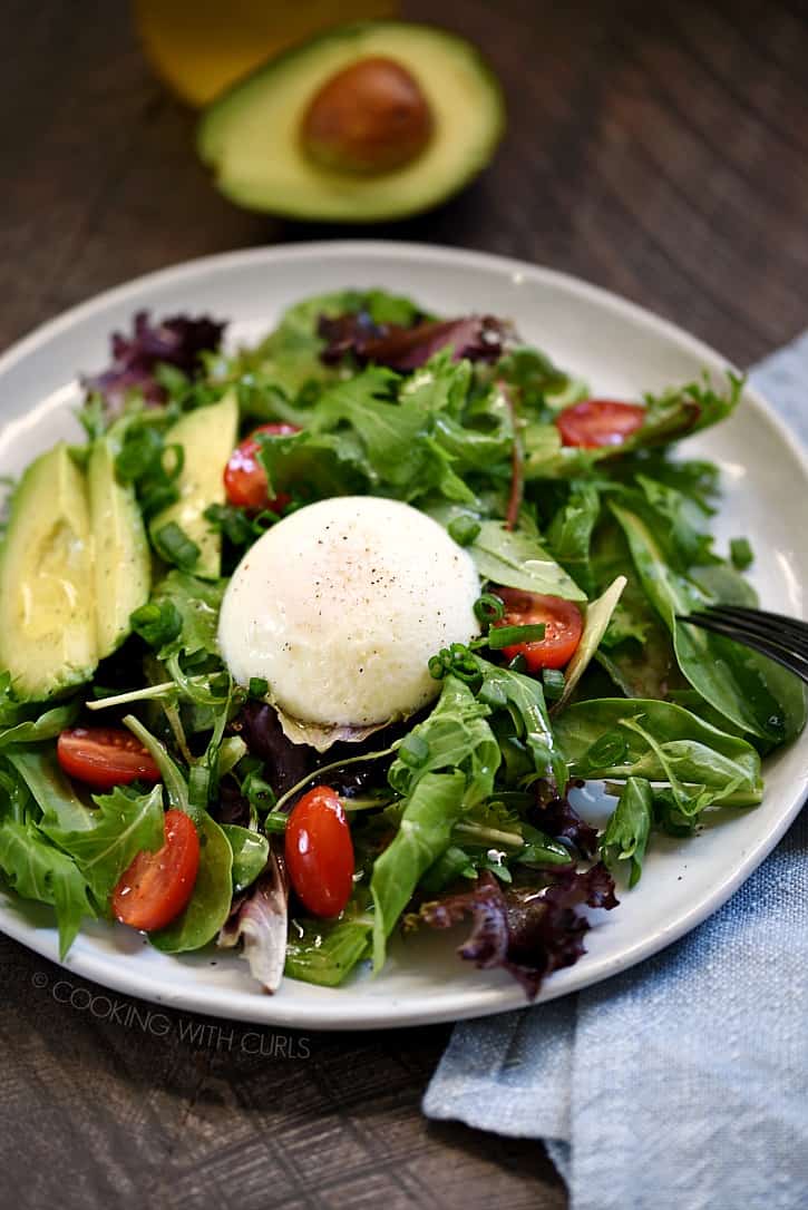 A poached egg on top of a green salad with cherry tomatoes and sliced avocado.
