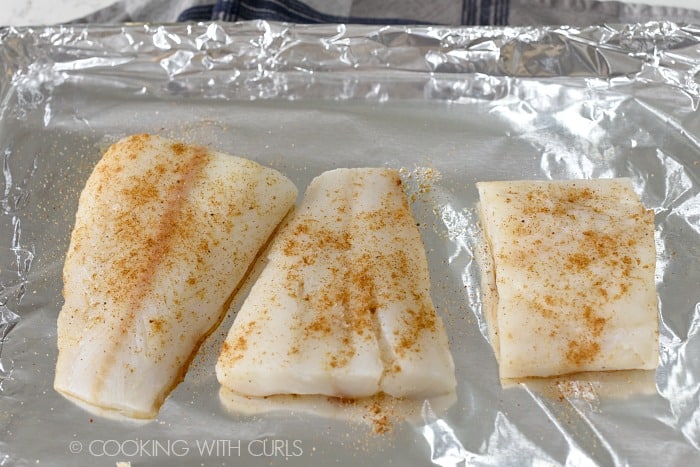 Seasoned fish on a foiled lined baking sheet.