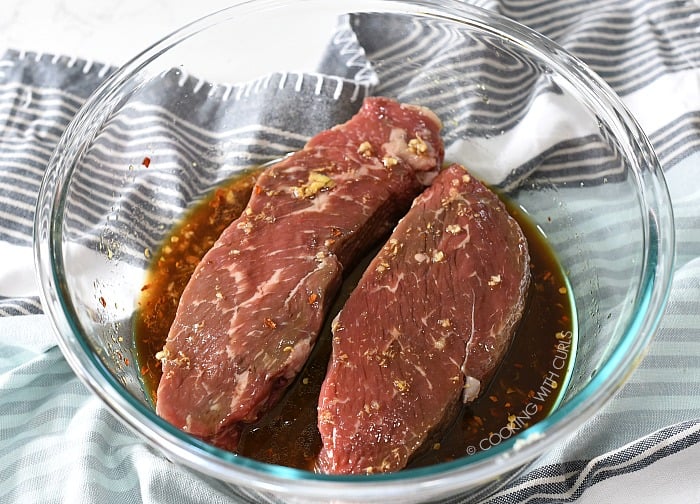 Sirloin steaks marinating in a large glass bowl cookingwithcurls.com