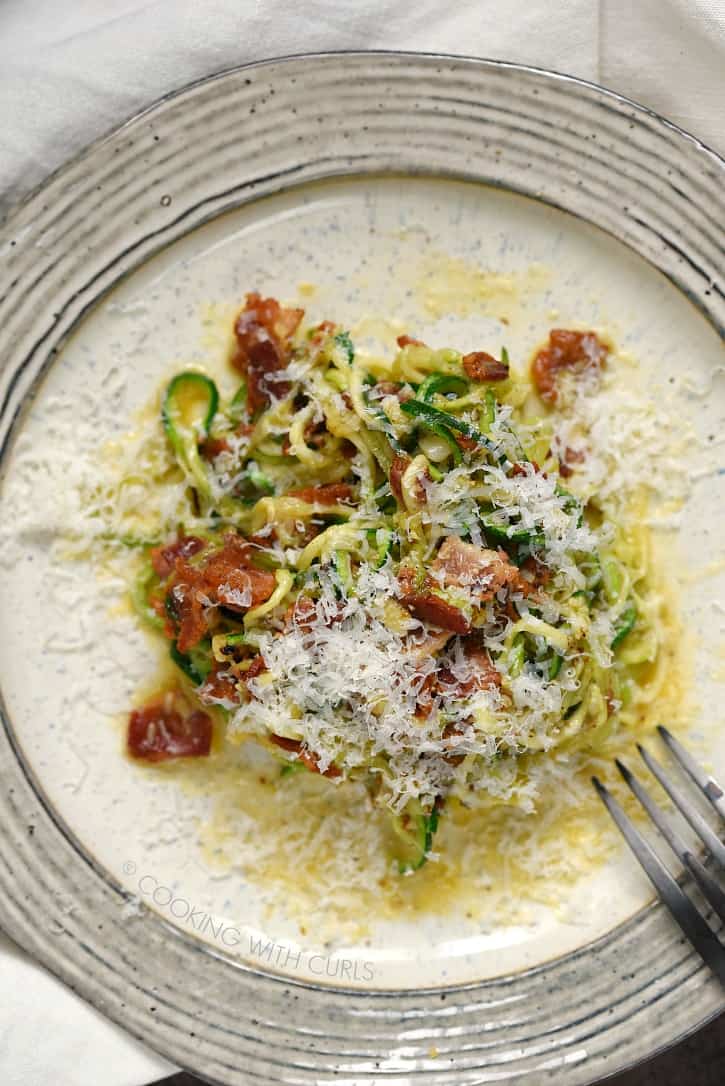 A creamy sauce, crispy bacon and grated Parmesan surround zucchini noodles to create the ultimate Zucchini Carbonara served on a beige plate