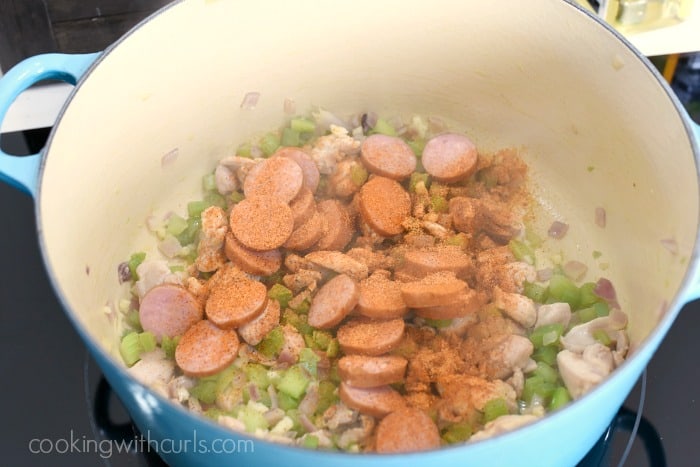 Cajun seasoning, sausage, chicken, bell pepper, onion and celery in a large blue pot on the stove