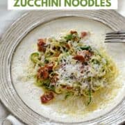 Zucchini noodles, parmesan and bacon pieces in a creamy egg sauce on a dinner plate with title graphic across the top.