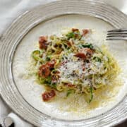 Zucchini noodles, parmesan and bacon pieces in a creamy egg sauce on a dinner plate.