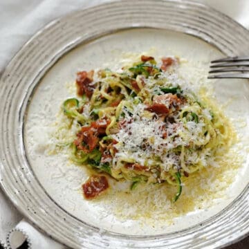 Zucchini noodles, parmesan and bacon pieces in a creamy egg sauce on a dinner plate.