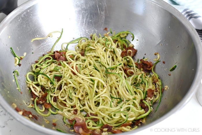 Zucchini noodles tossed with bacon, garlic, egg and Parmesan in a large stainless steel bowl 