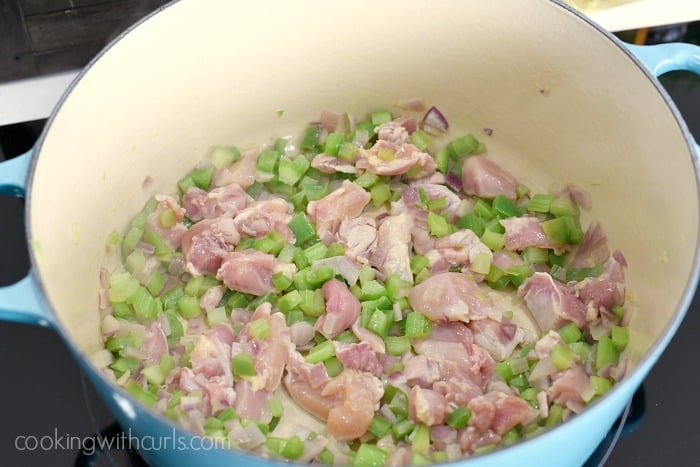 chopped chicken thighs sauteing in a large blue pot with celery, onions and green peppers
