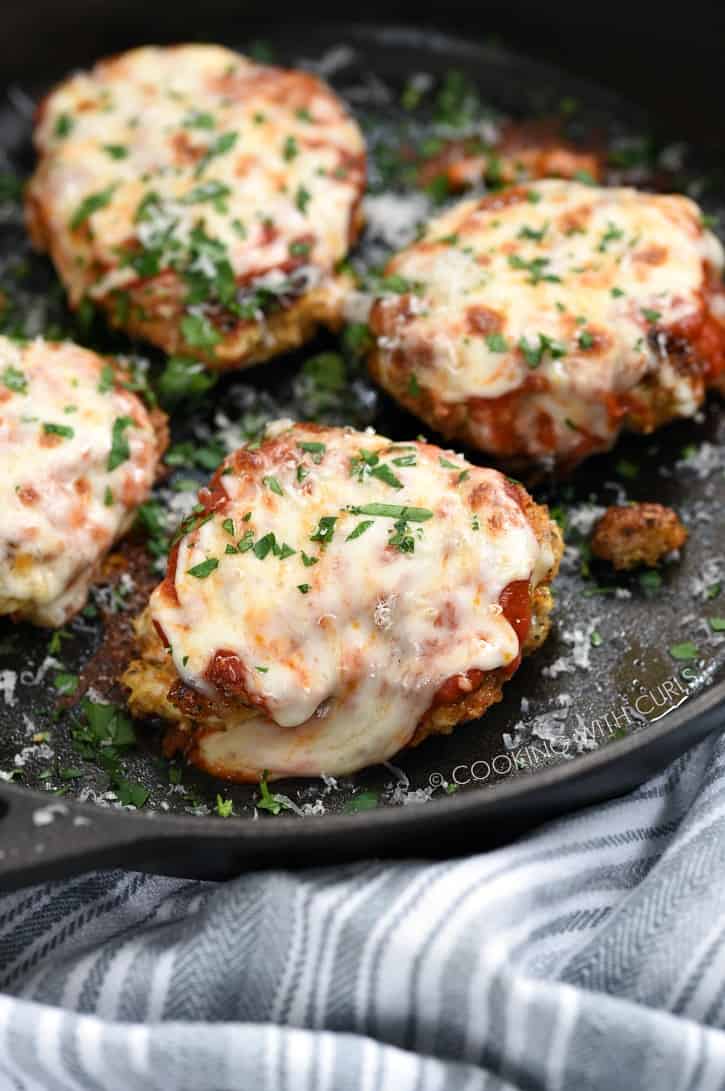 four cheese covered Parmesan crusted chicken breasts in a cast iron skillet
