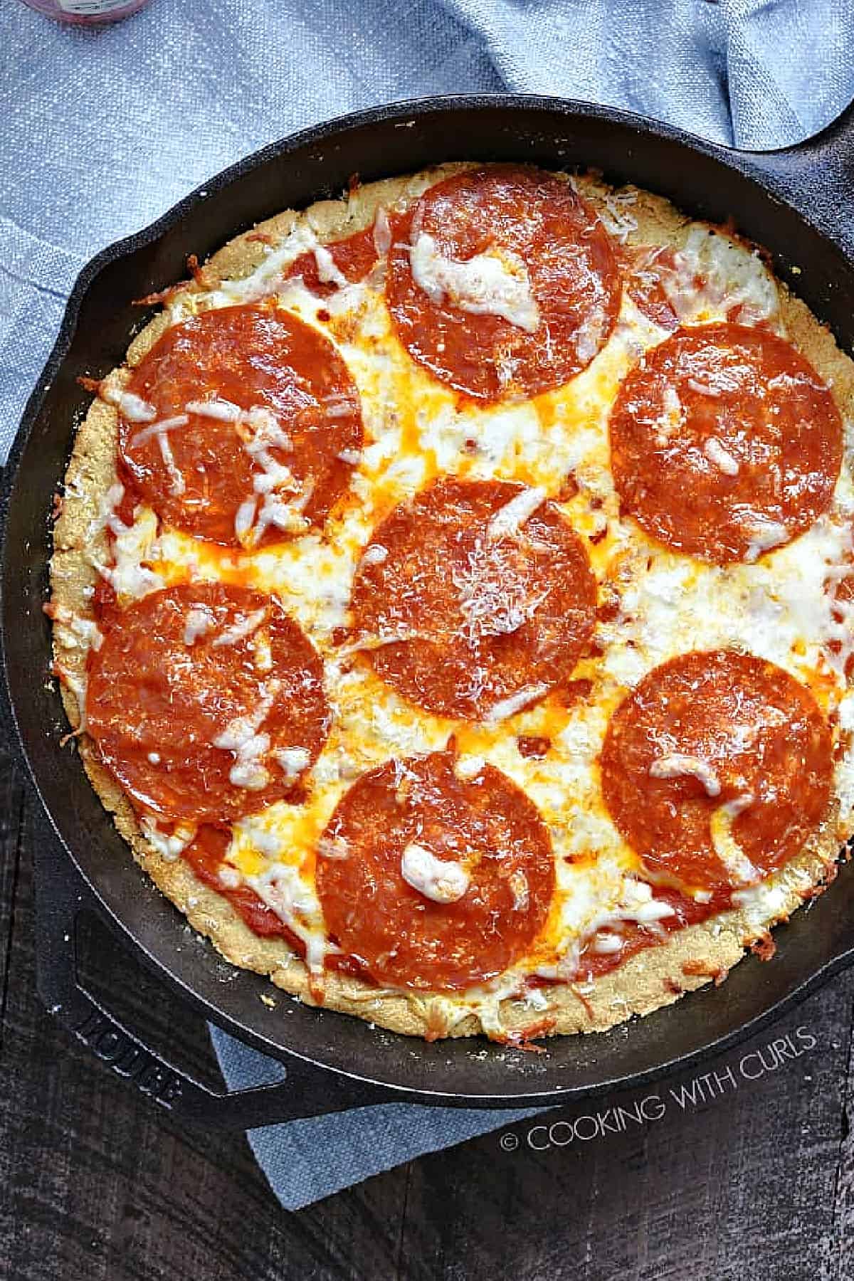Keto Pizza Crust topped with sauce, melted cheese and pepperoni in a cast iron skillet recipe. 