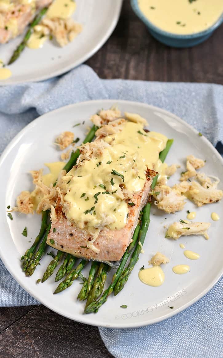 crab and sauce covered salmon filet on a bed of asparagus on a small white plate.