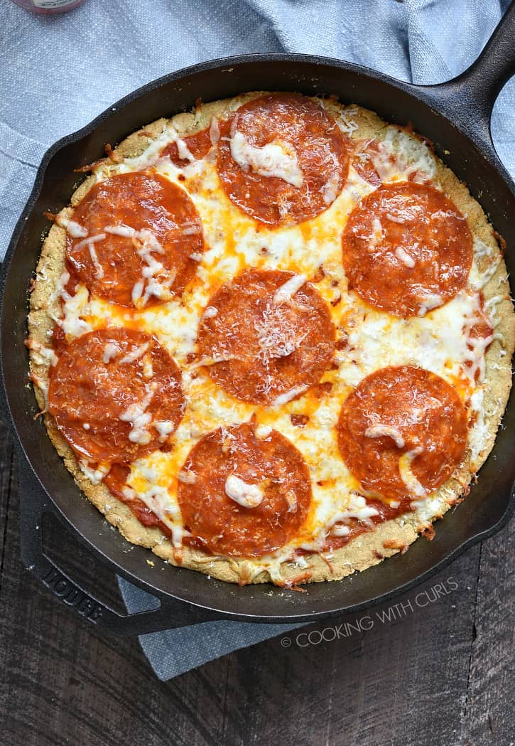 a blue napkin on a wooden board topped with a cast iron skillet pepperoni pizza