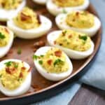 bacon ranch deviled eggs on a wooden plate sitting on a blue napkin