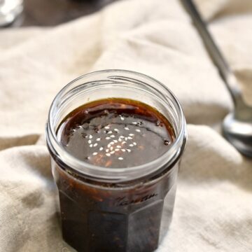 a small jar of sugar free teriyaki sauce on a beige linen napkin with a black spoon, salt and pepper shakers in the background