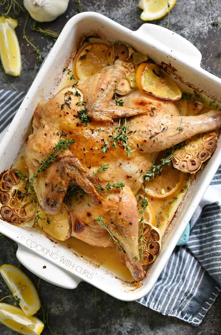 roasted spatchcock chicken in a white baking dish sitting on a blue and white striped napkin