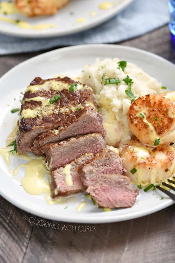 Sliced steak nestled into mashed cauliflower and seared scallops drizzled with lime-dill hollandaise on a white plate