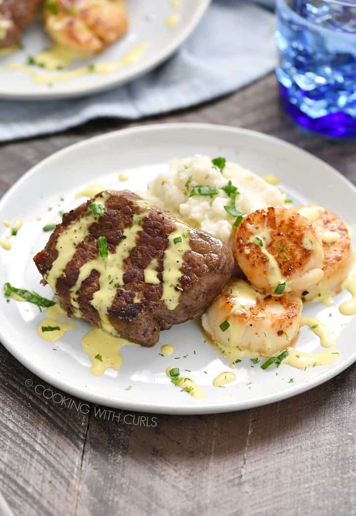 steak, scallops and mashed cauliflower on a white plate drizzled with hollandaise sauce