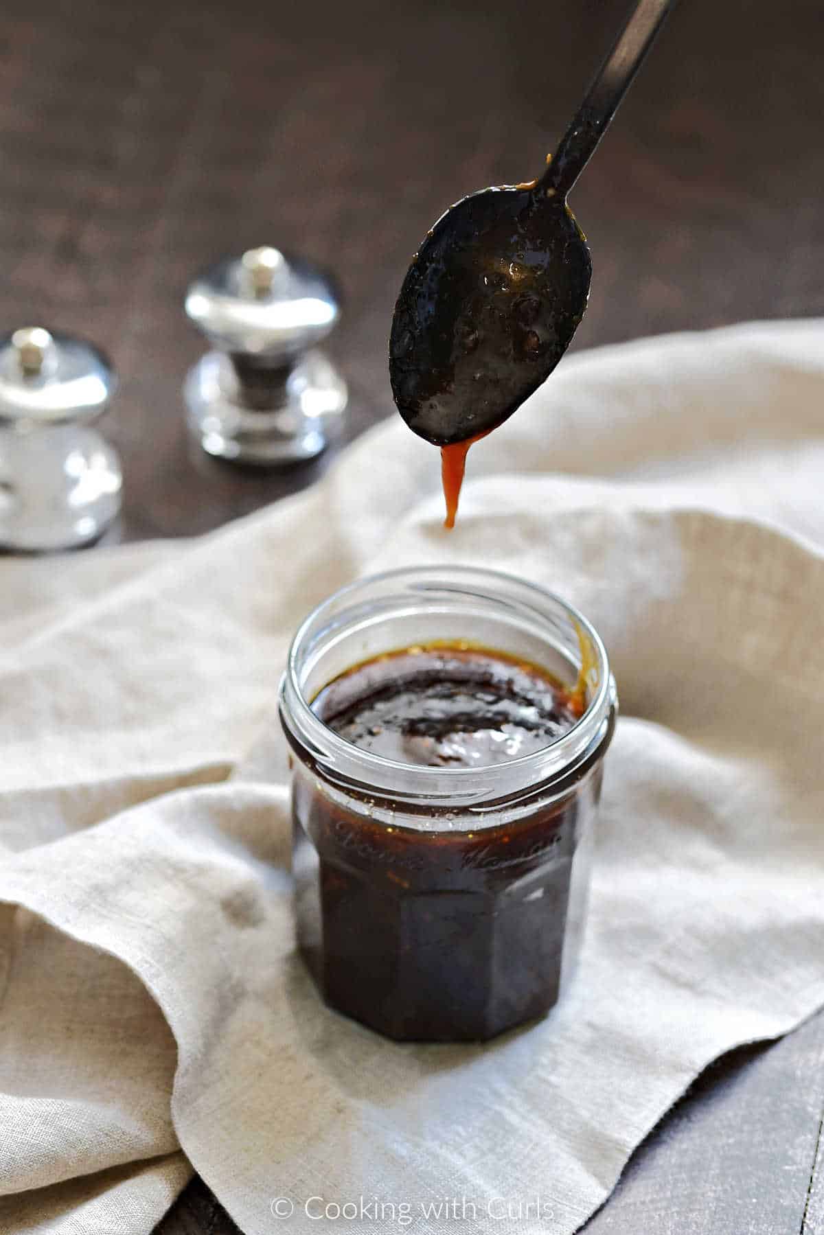 A black spoon dripping teriyaki sauce down into a glass jar of sauce.