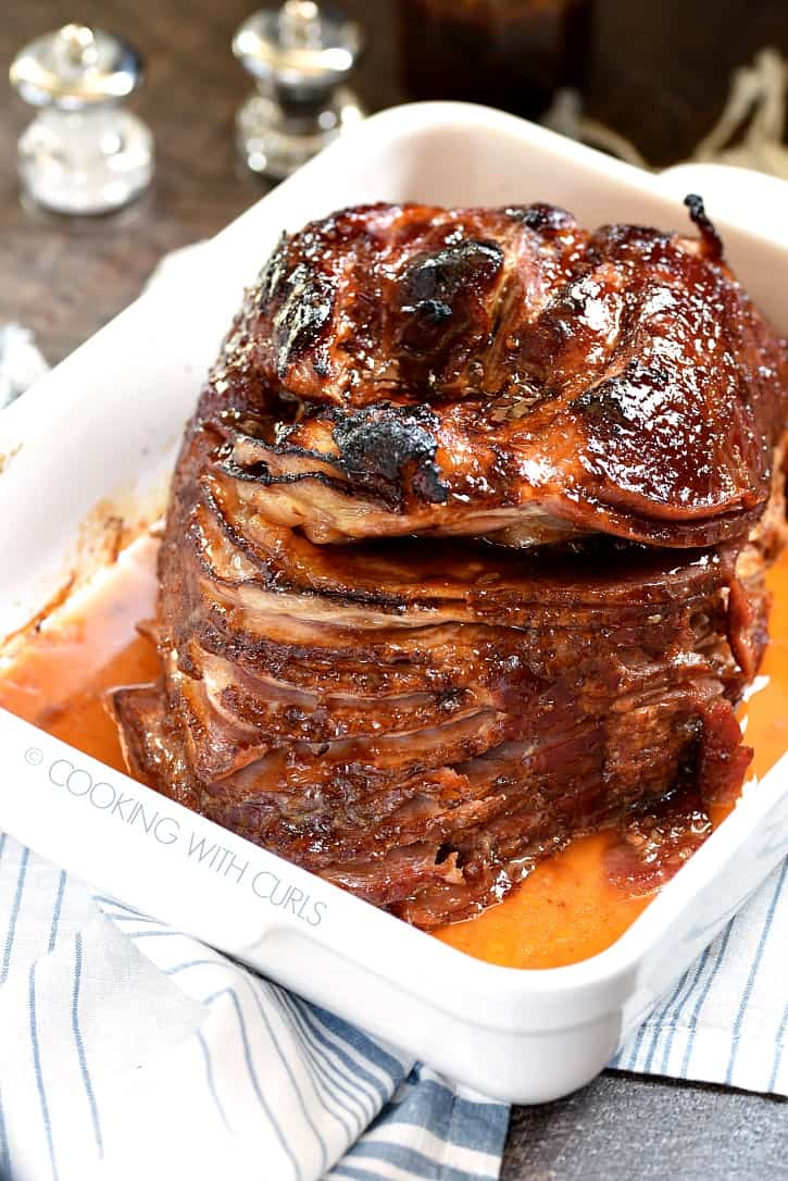 spiral glazed ham in a white, square baking dish sitting on a blue and white striped napkin with a salt and pepper shaker in the background