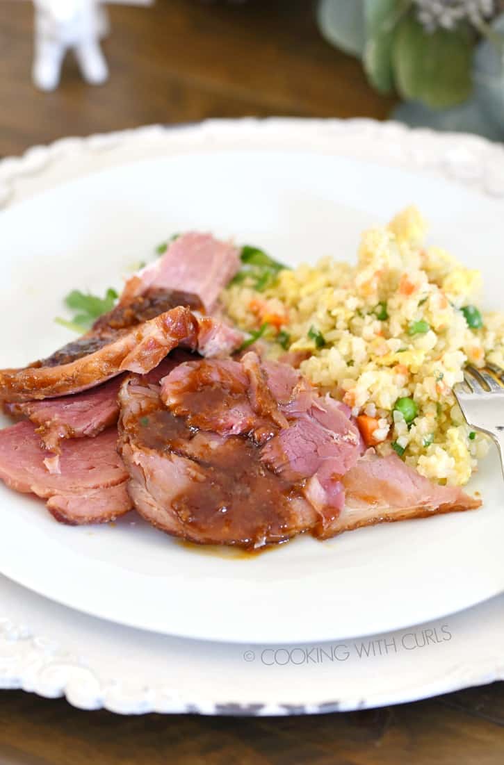 Sliced ham drizzled with glaze and fried rice on the side served on a dinner plate.