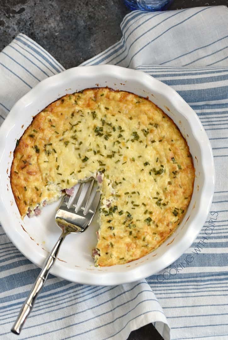 crustless ham and cheese quiche baked in a white pie plate with one slice removed and a serving fork in it's place