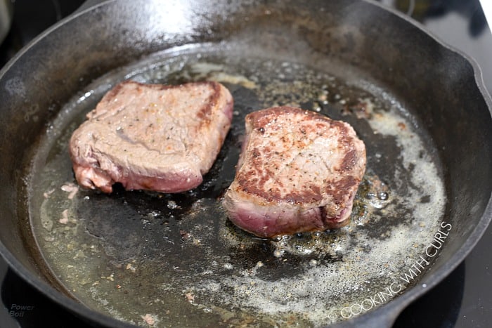Two seared steaks in a butter and oil coated cast iron skillet 
