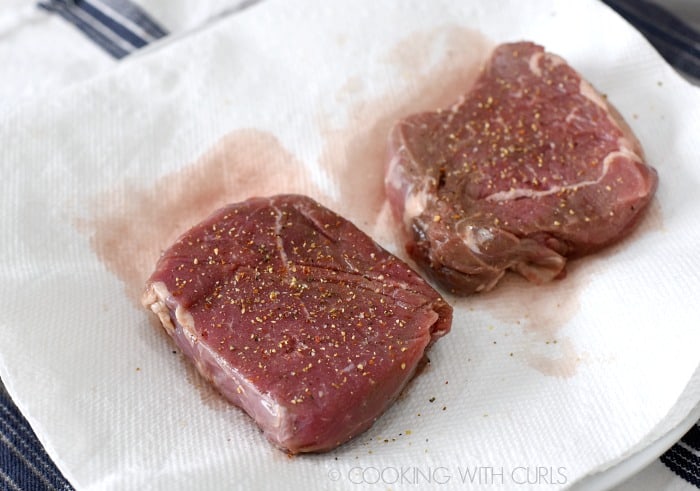 Two steaks seasoned with garlic pepper on a paper towel lined plate 