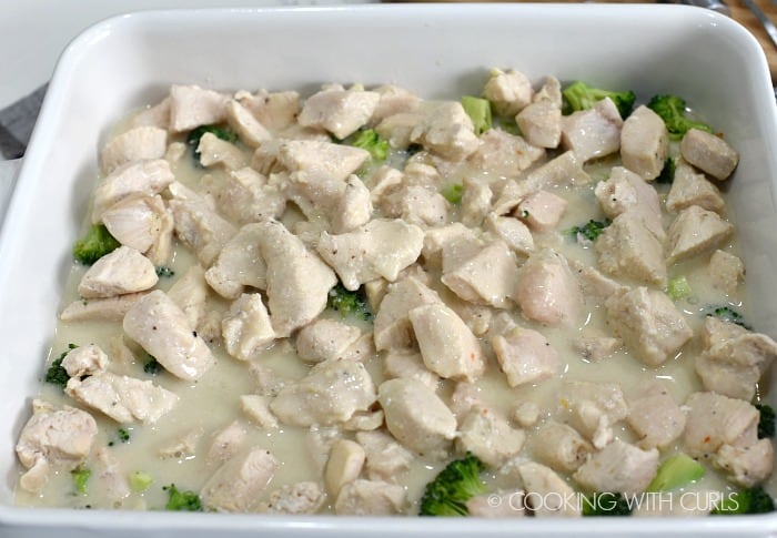 sauce poured over the chicken and broccoli in a white baking dish 