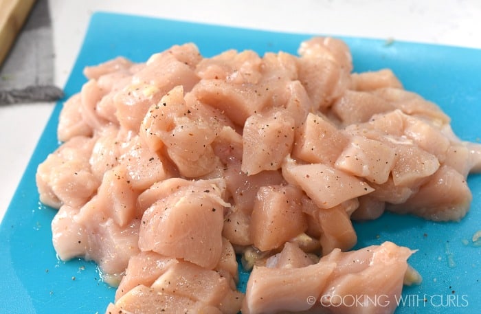 seasoned, chopped chicken breasts on a blue cutting mat 