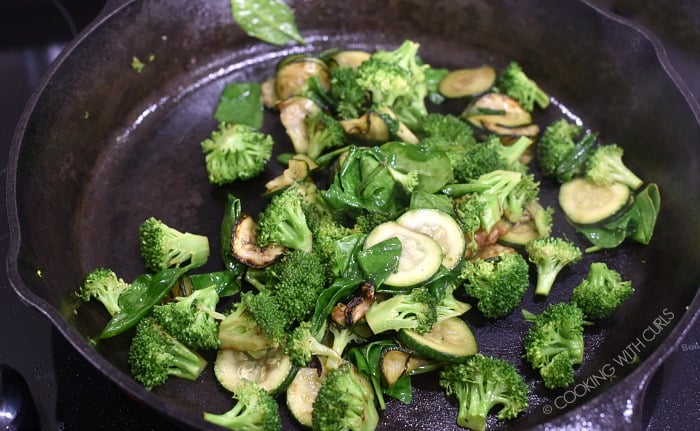 Broccoli, zucchini and spinach cooking in a cast iron skillet.