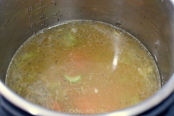 Chicken stock and seasonings added to the vegetables in the metal liner of a pressure cooker 