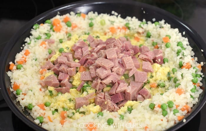 Chopped ham added to the scrambled eggs in the center of the pan with rice, carrots and peas 