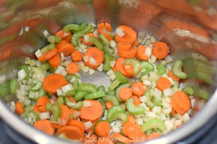 Diced onions mixed with sliced carrots and celery in the metal liner of a pressure cooker 