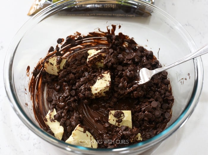 Partially melted chocolate chips and cocoa butter mixed together with a fork in a clear glass bowl