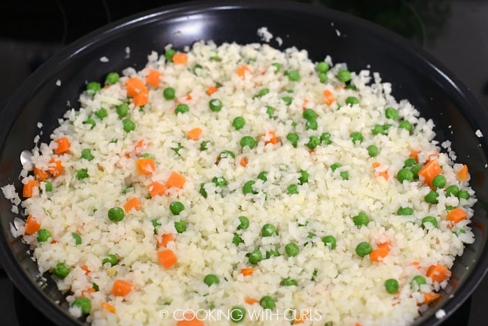 Rice, peas and carrots cooking in a large black skillet 
