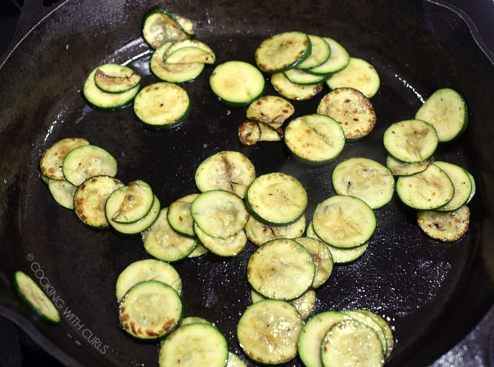 Thinly sliced zucchini cooking in a cast iron skillet.