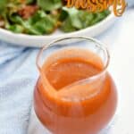Homemade French Dressing in a clear glass pitcher with a blue napkin and plate of salad in the background