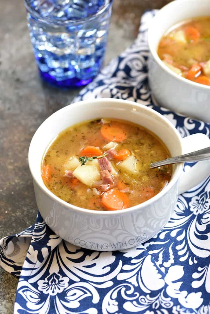 Two white bowls filled with Instant Pot Ham Bone and Potato Soup, sitting on a blue and white patterned napkin with a blue glass of water in the background