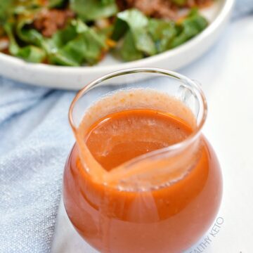Homemade French Dressing in a clear glass pitcher with a blue napkin and white plate with salad in the background