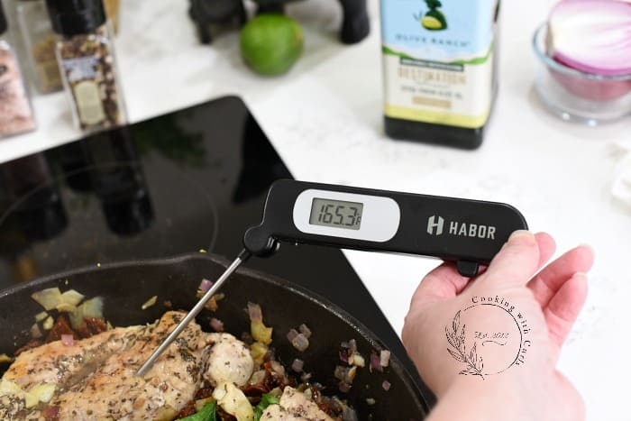 A 165.3 degree reading on a thermometer stuck into a piece of chicken in a cast iron skillet 