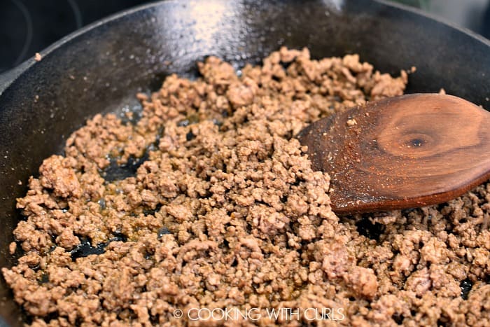 Browned, ground beef in a cast iron skillet with a wooden spatula on the right hand side 